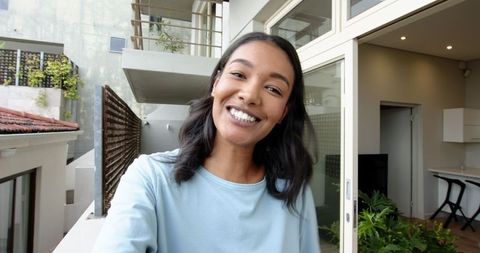 Smiling Woman Taking Selfie on Apartment Balcony Amid Potted Plants