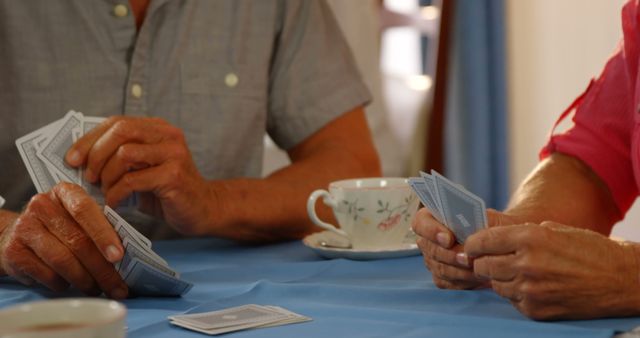 Senior adults enjoying a card game at home, showcasing leisure and social activities in retirement. Hands holding playing cards, creating a warm and engaging atmosphere perfect for illustrating content on senior lifestyles, social activities for the elderly, or family bonding moments.