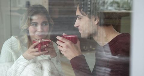 Cozy couple relaxing indoors sipping hot drinks by window