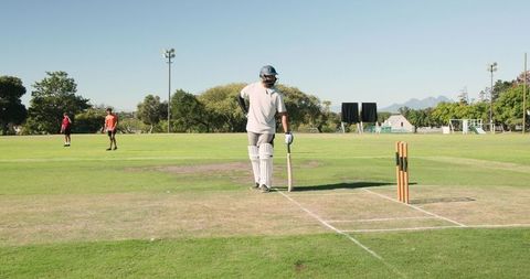 Cricket batter standing at crease with bat and stumps on sunny suburban sports field