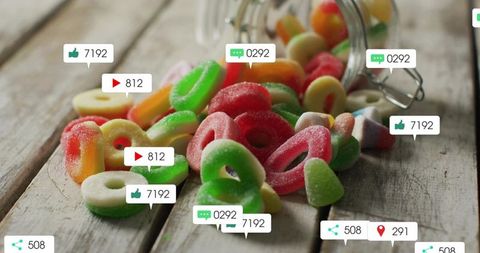 Colorful sugar-coated gummy rings spilling from glass jar on rustic wooden tabletop with social over