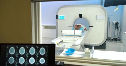 African american patient lying on ct scanner table sliding into gantry with brain scan monitor