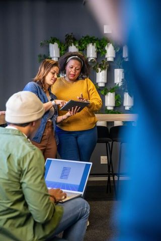 Diverse team collaborating over tablet in modern coworking space with greenery