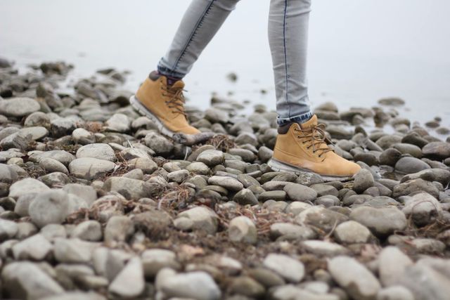 Person wearing yellow boots walking on rocky path in outdoor setting. Useful for themes involving outdoor activities, hiking, casual fashion, seasonal outfits, adventure lifestyle, nature exploration. Perfect for travel blogs, clothing advertisements, and websites focused on outdoor experiences.