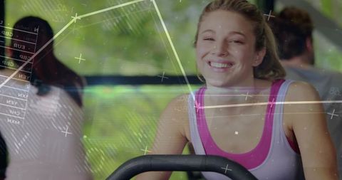 Smiling young woman pedaling stationary bike with futuristic HUD overlays in sunlit gym