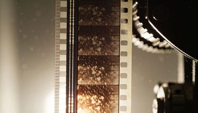 Vertical 35mm film strip threading through vintage projector gear with scratches