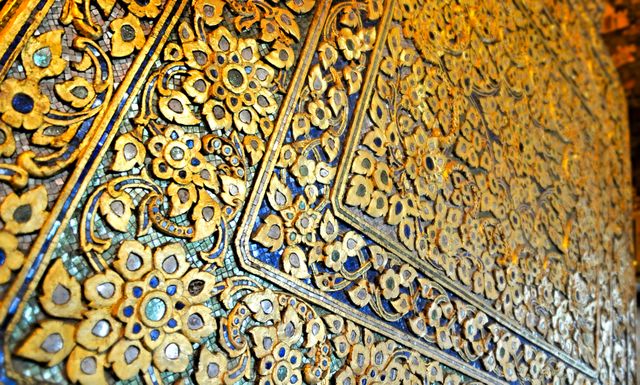 Intricate golden floral pattern on a wall showcasing traditional Asian design. Highlights ornate details and exquisite craftsmanship, making it ideal for backgrounds, cultural art presentations, and design inspiration. Perfect for use in publications related to Asian art, interior design, and luxurious decor themes.