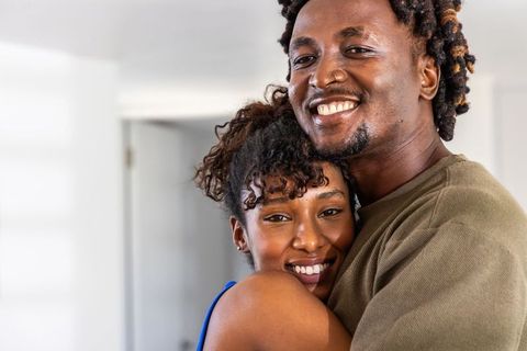African american couple embracing and smiling in cozy home interior, joyful portrait