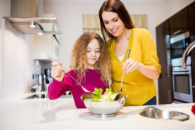 Mother assisting daughter in making salad in kitchen