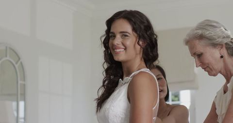 Bride smiling while mother helps adjust wedding dress