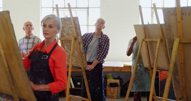 Senior adults attending a painting class at an art studio, standing in front of easels and focusing on their artwork. This can be used for materials promoting senior education, creative classes, workshops for elderly people, or features on lifelong learning and hobbies.