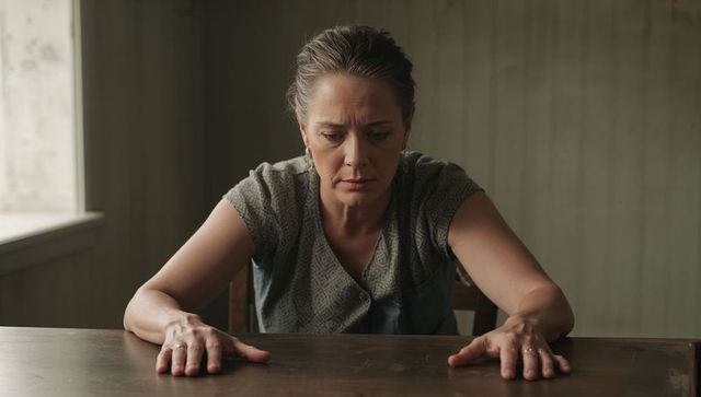 Woman leaning on worn wooden table, contemplating in minimalist home interior