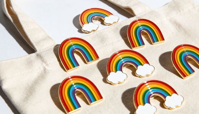 Colorful rainbow enamel pins decorating canvas tote bag with gold outlines and natural shadows