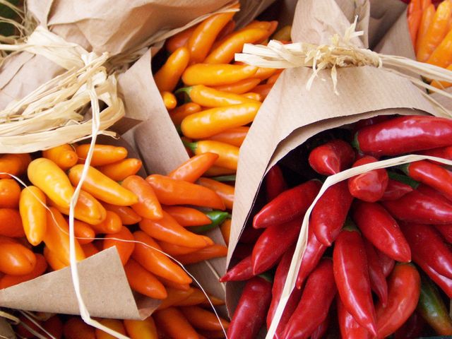 Bunches of bright orange and red chili peppers are wrapped in rustic brown paper, creating a colorful and vibrant display. This scene evokes a fresh market vibe and showcases the natural beauty of fresh produce. Ideal for use in content related to cooking, food markets, agriculture, natural eating, and exploring exotic food ingredients.
