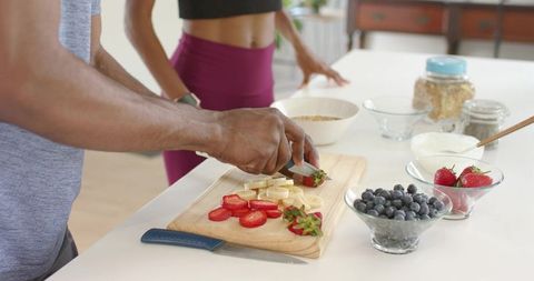 Couple preparing healthy breakfast cutting strawberries and bananas for yogurt and oats