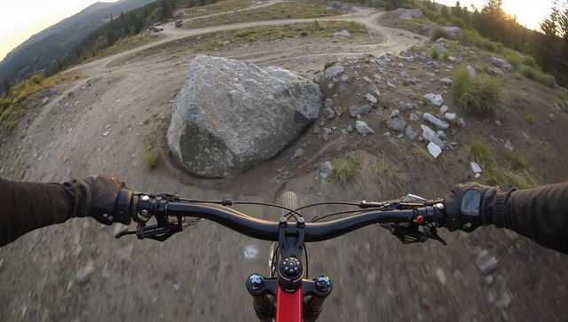 First-person mountain biking downhill hands-on handlebars navigating rocky trail at sunset