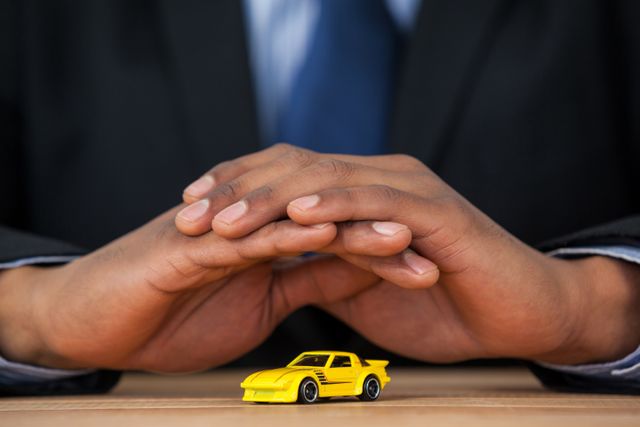 Businessman in suit protecting yellow toy car with hands. Ideal for concepts related to insurance, safety, security, risk management, and financial protection. Useful for advertisements, blogs, and articles on business responsibility and investment strategies.