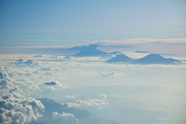 Aerial view showcasing mountain peaks emerging through a dense cloud layer during sunrise. The expansive sky and misty cloud cover create a serene and tranquil atmosphere. Perfect for use in travel brochures, nature magazines, inspirational posters, and desktop wallpapers.