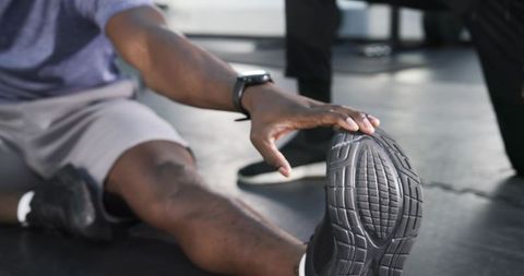 Athletic man stretching hamstring on gym floor with coach