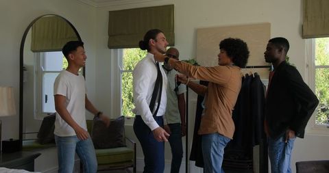 Groom preparing for wedding with friends smiling together