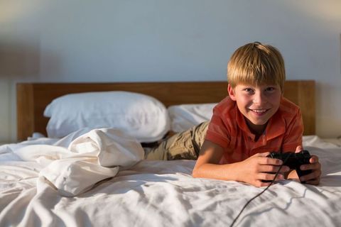 Smiling Boy Playing Video Games on Bed in Casual Setting