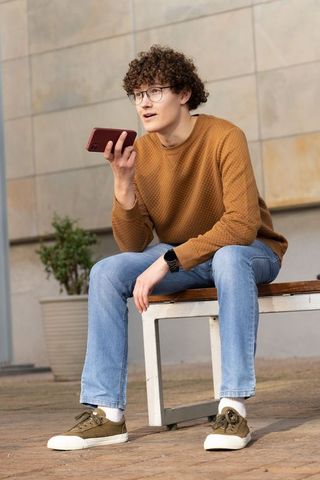 Young man talking into smartphone while sitting on urban bench wearing brown sweater