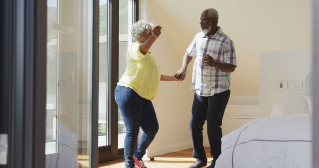 Happy senior diverse couple dancing in living room at retirement home. healthy, active retirement and body inclusivity.