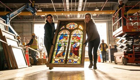 Women carrying stained glass panel in industrial restoration workshop, careful handling