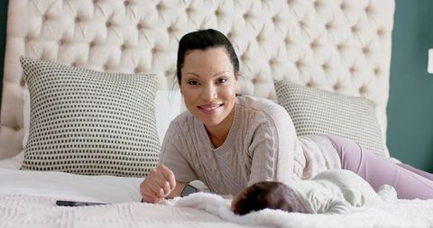 Happy mother relaxing with infant in cozy bedroom with tufted headboard