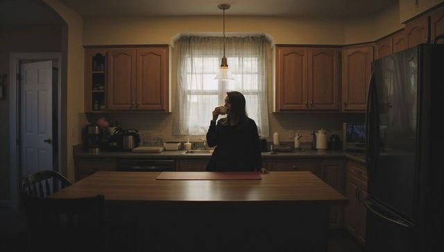 Woman sipping coffee at kitchen island in warm rustic wooden kitchen