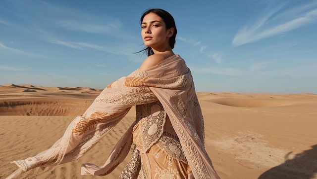 Elegant model in lace gown poses amidst expansive desert dunes