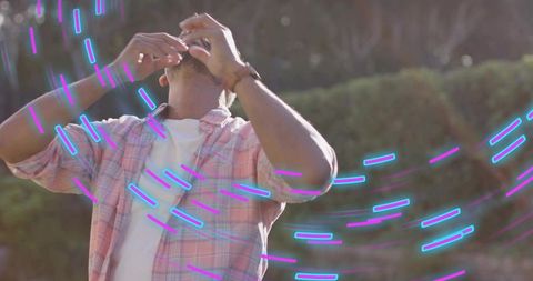Backlit man in pink plaid shirt surrounded by neon cyan purple light trails, vibrant motion