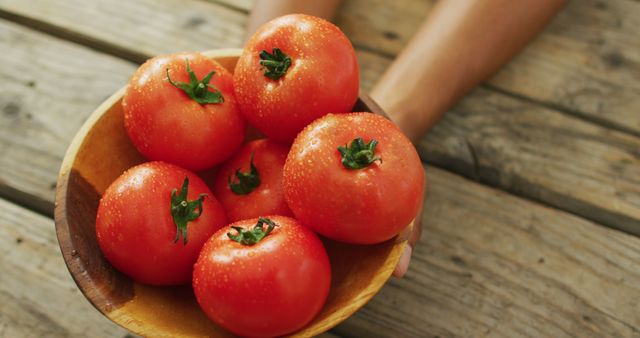 Bright, fresh tomatoes sitting in a wooden bowl displayed on a rustic wooden table. Ideal for use in articles and advertisements focusing on healthy eating, organic produce, farming, and gardening. Perfect for food blogs, cookbooks, and nutrition websites.