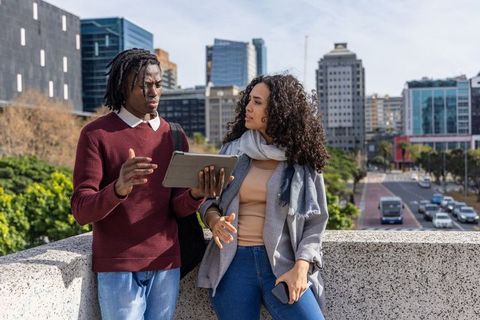 Young professionals reviewing tablet and discussing urban business strategy on city bridge