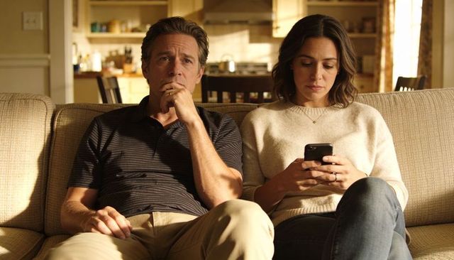 Couple sitting on sofa showing emotional distance while woman scrolling smartphone