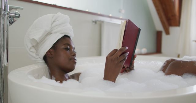 Features a woman with a towel on her head, comfortably soaking in a bubble bath while reading a book. Suitable for content about relaxation, self-care routines, leisure activities, and mental wellness. Great for advertisements, blogs, and social media posts highlighting stress relief and pampering moments.