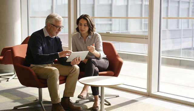Senior executive mentoring on tablet in modern office lounge with floor-to-ceiling windows