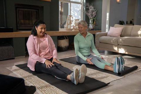 Mature women stretching together in cozy living room practicing gentle home fitness