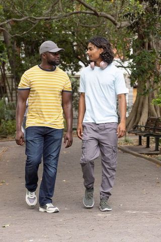 Diverse friends walking and talking in urban park wearing headphones and baseball cap