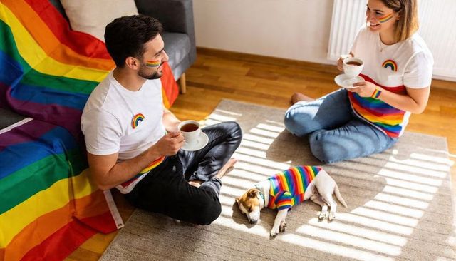 Couple celebrating pride at home, sharing morning coffee with rainbow dog