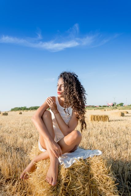 Woman Sitting on Hay Bale in Sunlit Field - Download Free Stock Photos Pikwizard.com