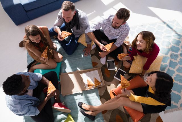 Group of diverse colleagues sitting on floor, enjoying pizza during office break. Ideal for illustrating teamwork, office culture, casual meetings, and employee bonding. Suitable for use in articles about workplace dynamics, team building activities, and corporate culture.