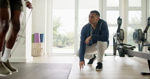Personal trainer coaching male trainee jumping rope in bright home gym with rowing machines