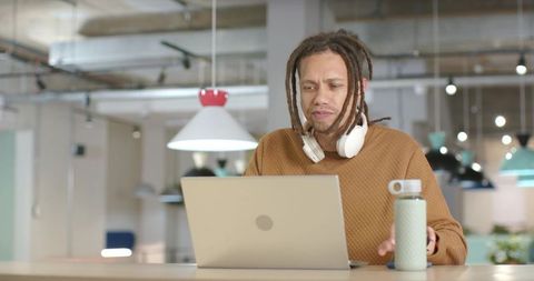 African American man working on laptop in modern coworking space with headphones