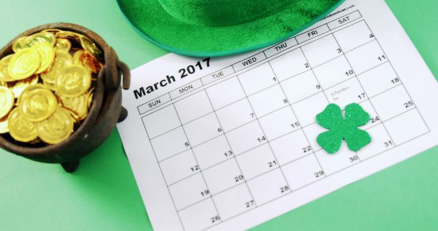 A pot of gold coins and a green hat rest near a calendar marked with St. Patrick's Day, with copy space. These items symbolize the celebration of the Irish holiday, known for its themes of luck and prosperity.