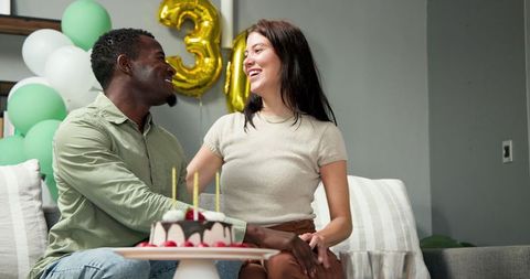 Joyful couple celebrating birthday with cake and balloons indoors