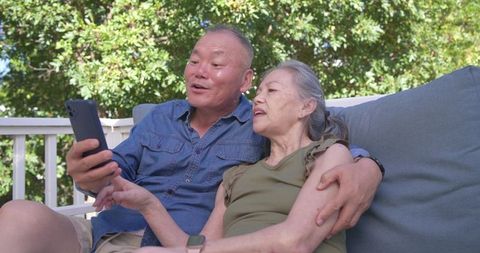 Senior couple relaxing on sunny deck couch sharing smartphone and enjoying moment