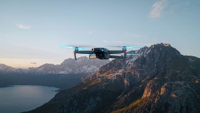Folding drone hovering over alpine lake and sunlit mountain ridges with camera gimbal