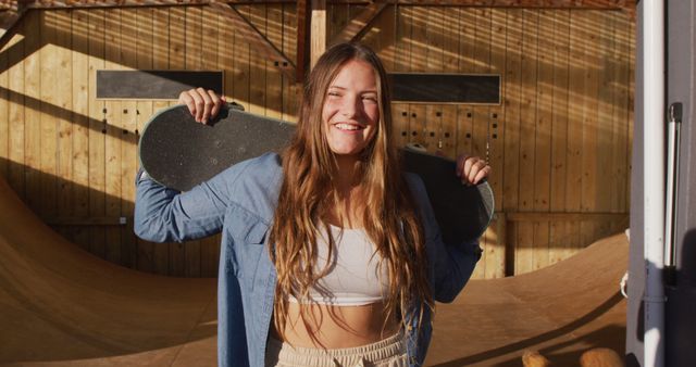 Image of happy caucasian female skateboarder holding skateboard in skate park. Skateboarding, sport, active lifestyle and hobby concept.