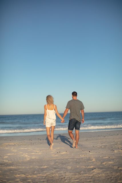 Rear view of couple walking together hand in hand on the beach